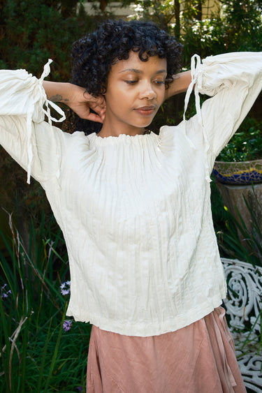 Woman wearing a white blouse with ruffled sleeves in an outdoor setting