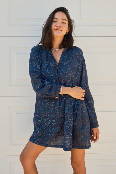 Woman standing in front of a white garage door wearing a navy blue tapestry mini shirt dress with long sleeves.