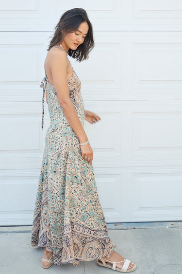 A woman standing in front of a white garage door, wearing a multicolored floral Nova slip dress. Side view