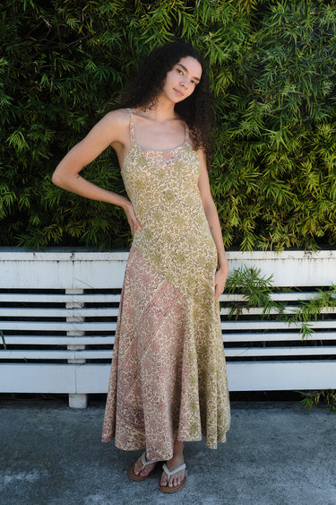 A woman wearing a mixed print slip dress of pea and blush calico tapestry, posing outdoors.