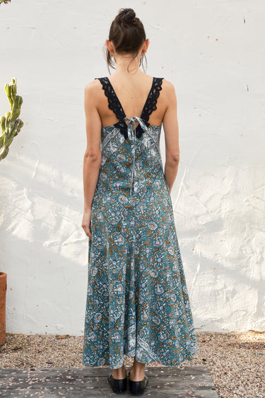 Woman wearing a floral dress with lace straps against a white wall.