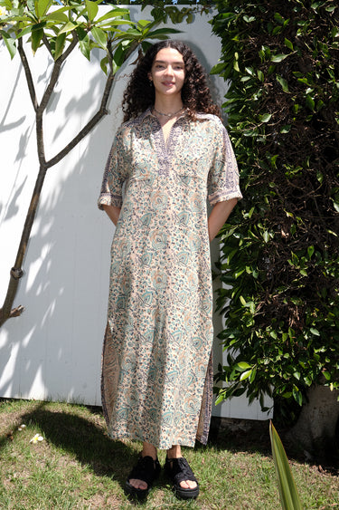 A woman standing outdoors wearing a floral print maxi dress with a shirt collar and sleeves, featuring a handloom Indian Tapestry fabric.