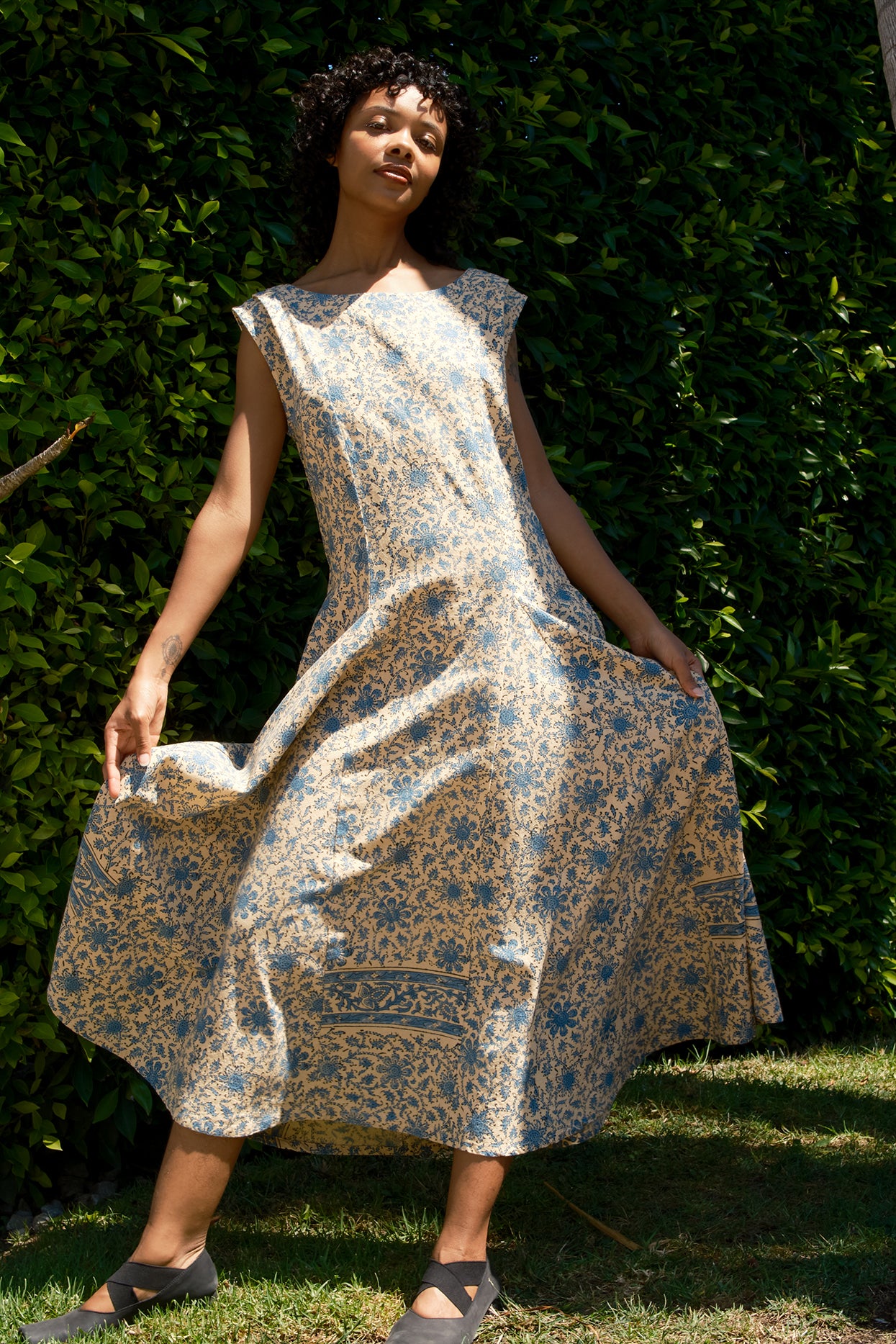 Woman wearing a floral dress standing against a green hedge