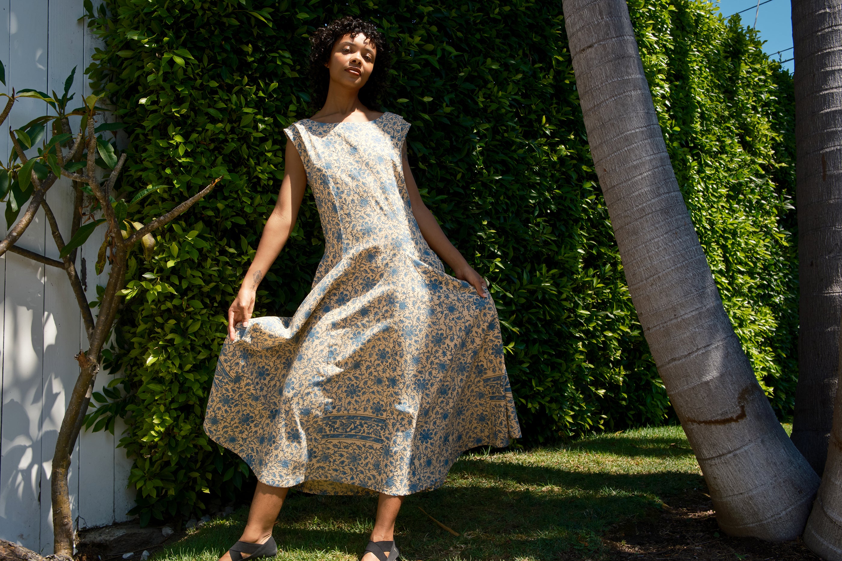 Woman in a floral dress standing outdoors with greenery in the background