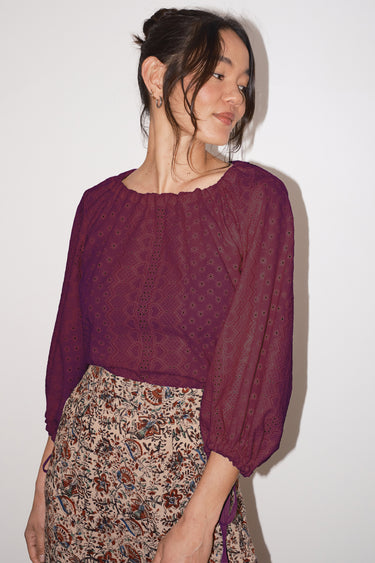 Woman wearing a eyelet patterned blouse and floral skirt against a white background