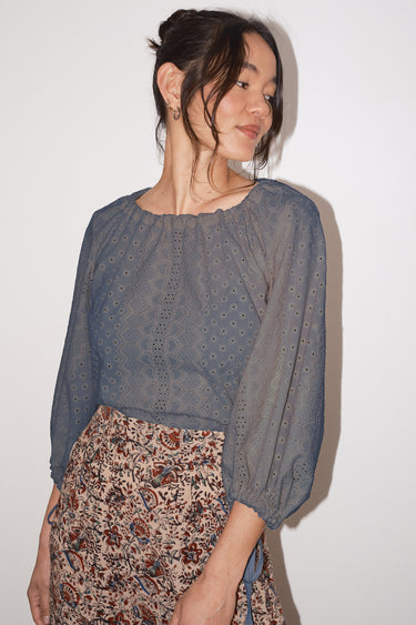Woman wearing a pewter eyeletblouse and floral skirt against a white background