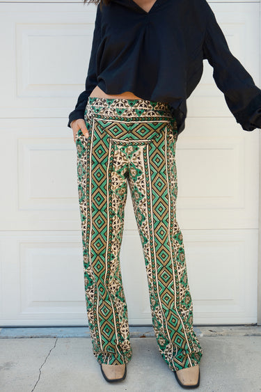 A person wearing a flare legged full length pant with a mid rise and a hand block printed Indian Tapestry design.