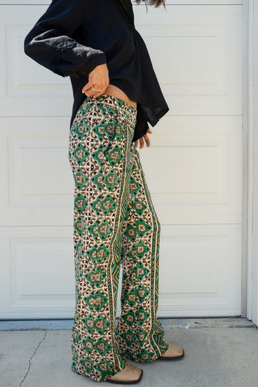 A person wearing a flare legged full length pant with a mid rise and a hand block printed Indian Tapestry design.