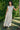 Woman in a floral dress standing against a green hedge