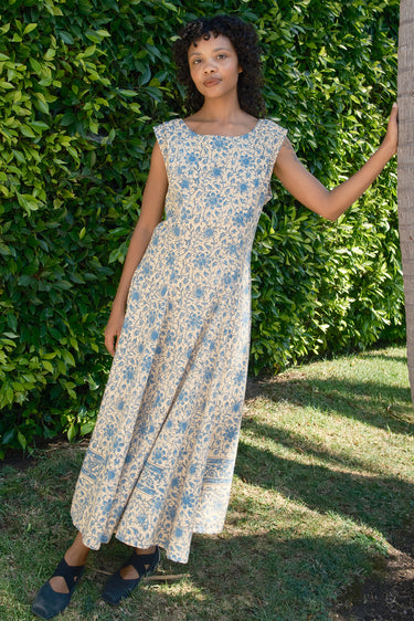 Woman in a floral dress standing against a green hedge