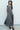 Woman wearing a gray dress standing in front of a white wall.
