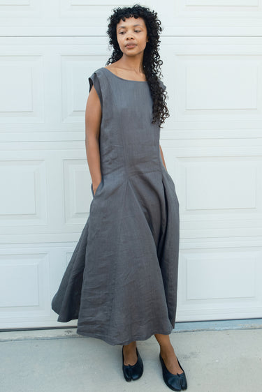 Woman wearing a gray dress standing in front of a white wall.