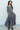Woman wearing a gray dress standing against a white wall.