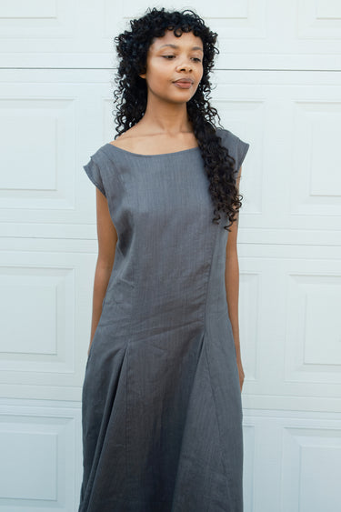 Woman wearing a gray dress standing against a white wall