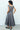 Woman wearing a gray dress standing against a white wall.