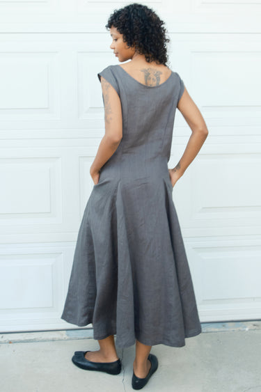 Woman wearing a gray dress standing against a white wall.