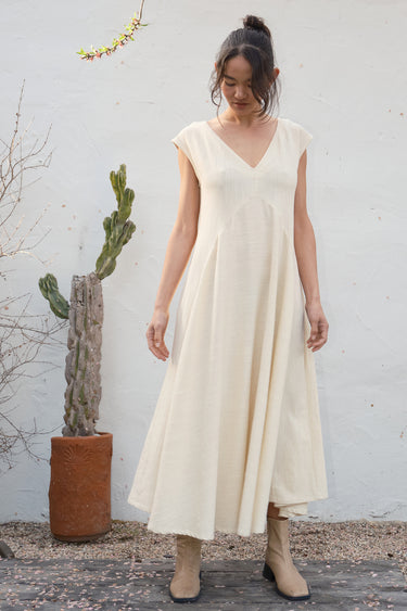 Woman in a alabaster dress standing outdoors with a white wall and cactus in the background.