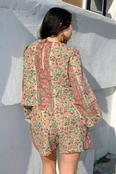 A woman standing outside wearing a floral print blouse tapestry blouse with a matching short, back view.