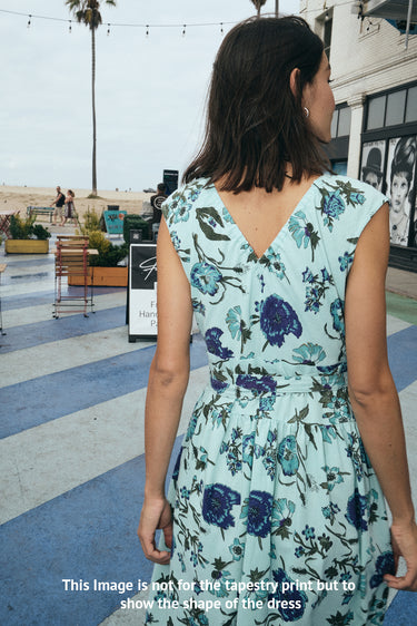 Woman wearing a floral dress in an outdoor setting with palm trees and buildings.