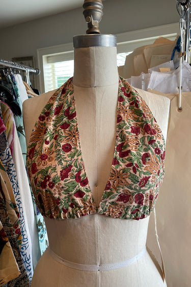 A halter style bikini top with a floral pattern in red and green on an ecru background, displayed on a dress form.