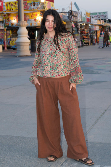 A woman standing at a beach boardwalk wearing a nutmeg brown trouser and a floral print blouse.
