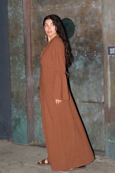 A woman standing by a metal door wearing a nutmeg brown zip front long sleeve dress.