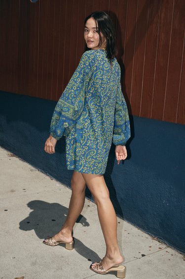 woman walking outside wearing a dark blue paisley tapestry mini dress with long sleeves. Side Back View
