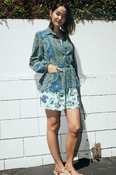 A woman standing outside wearing an aqua ground floral tapestry short with dark blue paisley jacket.