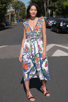 A woman standing on the sidewalk wearing a floral tapestry midi dress with an elastic neckline and pockets.