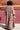 A woman standing by a red wall, outside wearing a long sleeve maxi caftan cut in a raisin floral tapestry, back view.