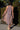 A woman standing in front of greenery outside wearing a sleeves midi caftan cut in a blue floral tapestry. Back View.