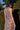 A woman standing in front of greenery outside wearing a sleeves midi caftan cut in a blue floral tapestry, belted.