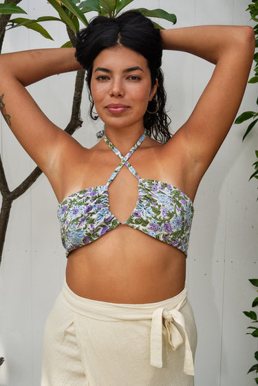 A woman wearing a white ground, lavender and blue floral tapestry bandeau bikini top and an alabaster skirt with a tie at the waist.