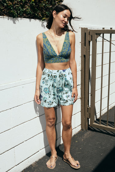A woman standing outside wearing a dark blue paisley tapestry bra top with aqua ground floral tapestry short