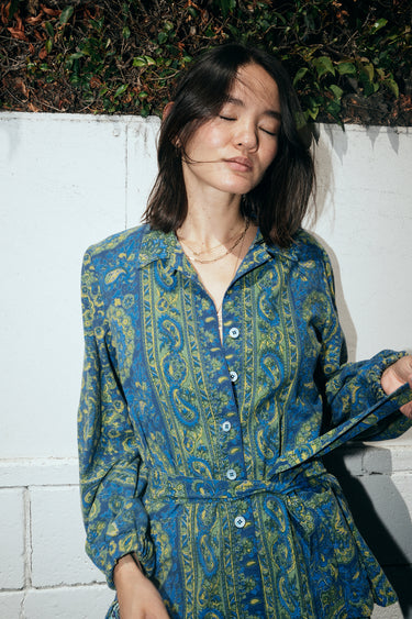 A woman standing outside by a wall wearing a shirt jacket cut from a dark blue paisley tapestry.