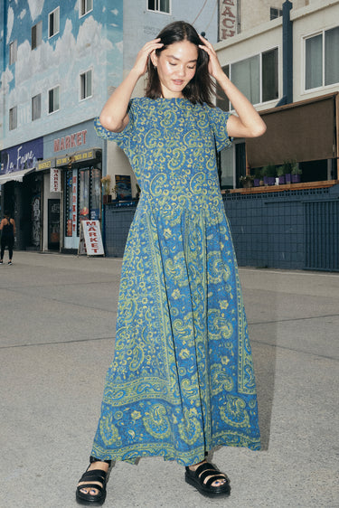 A woman at a beach boardwalk wearing a dark blue paisley tapestry maxi dress with pockets in the gathered skirt.
