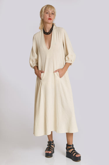 A woman standing in a white wall photo studio wearing a 3/4 sleeve midi alabaster off white caftan.