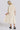 A woman standing in a white wall photo studio wearing a 3/4 sleeve midi alabaster off white caftan. Back View
