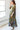 A woman standing in a studio with white walls wearing a maxi caftan cut in an olive green tree of life handloom tapestry. side view