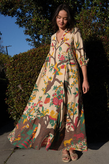 A woman standing outside by greenery wearing a maxi caftan cut in a tree of life handloom tapestry.