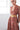 A woman in a studio with white walls wearing a red with blue flowers tapestry caftan with long sleeves. Close up, with gold belt.