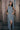 A model wearing a gray maxi shift dress with a front zipper and pockets, standing near a wooden fence.