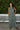 A woman standing outdoors with greenery wearing a green and brown floral patterned tapestry maxi sheath with broomstick pleats.