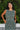 A woman standing outdoors with greenery wearing a green and brown floral patterned tapestry maxi sheath with broomstick pleats, belted.