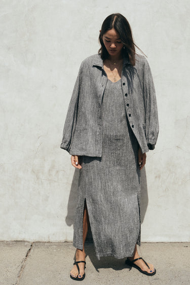 A gray unlined jacket with big patch pockets and an elastic shirred sleeve cuff, worn by a model facing away from the camera. She is wearing the jacket with a matching sheath dress.