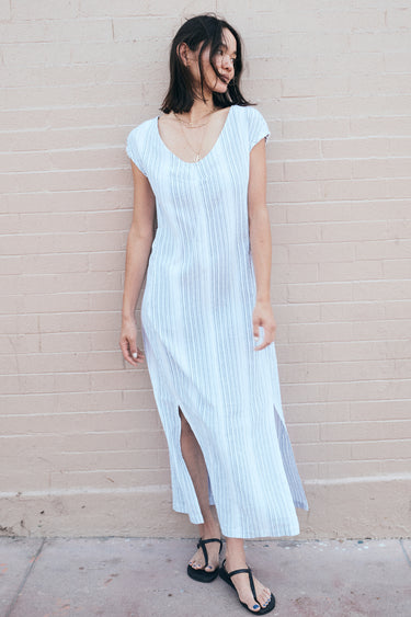 a woman standing by a pink wall wearing a long sheath dress cut for white gauze with a black pencil stripe.