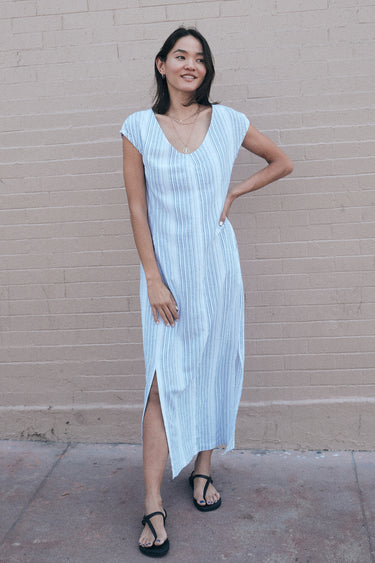 a woman standing by a pink wall wearing a long sheath dress cut for white gauze with a black pencil stripe.