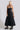 A model wearing a black circular maxi slip dress standing in a phot studio with white walls, the dress is belted.