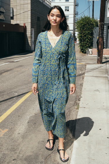A woman standing in the street wearing a long sleeve blue paisley tapestry midi wrap dress.