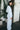 A woman outside wearing a long sleeved white with black stripe gauze shirt jacket with a matching trouser, side view.